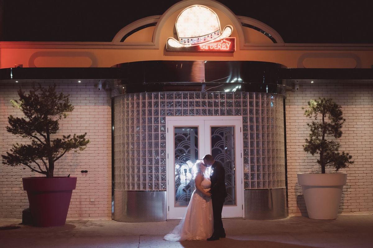 Newlyweds backlit in the glowing entrance of the Retro Suites Hotel at night, wedding portrait