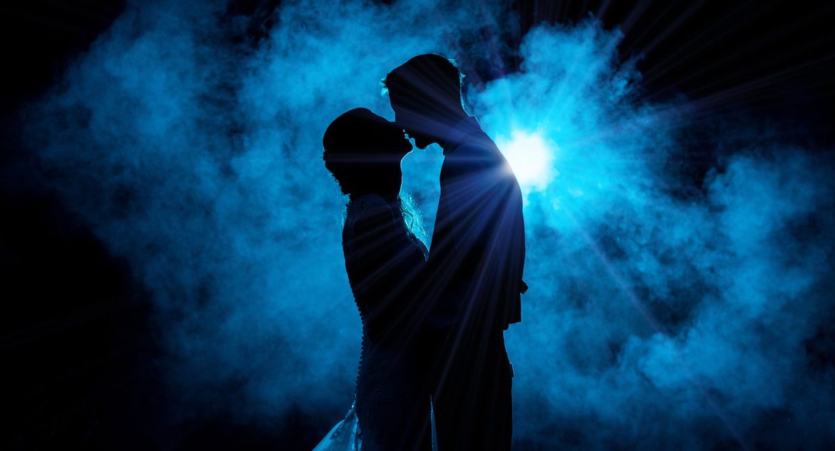 Silhouette of a bride and groom in glowing blue smoke at night