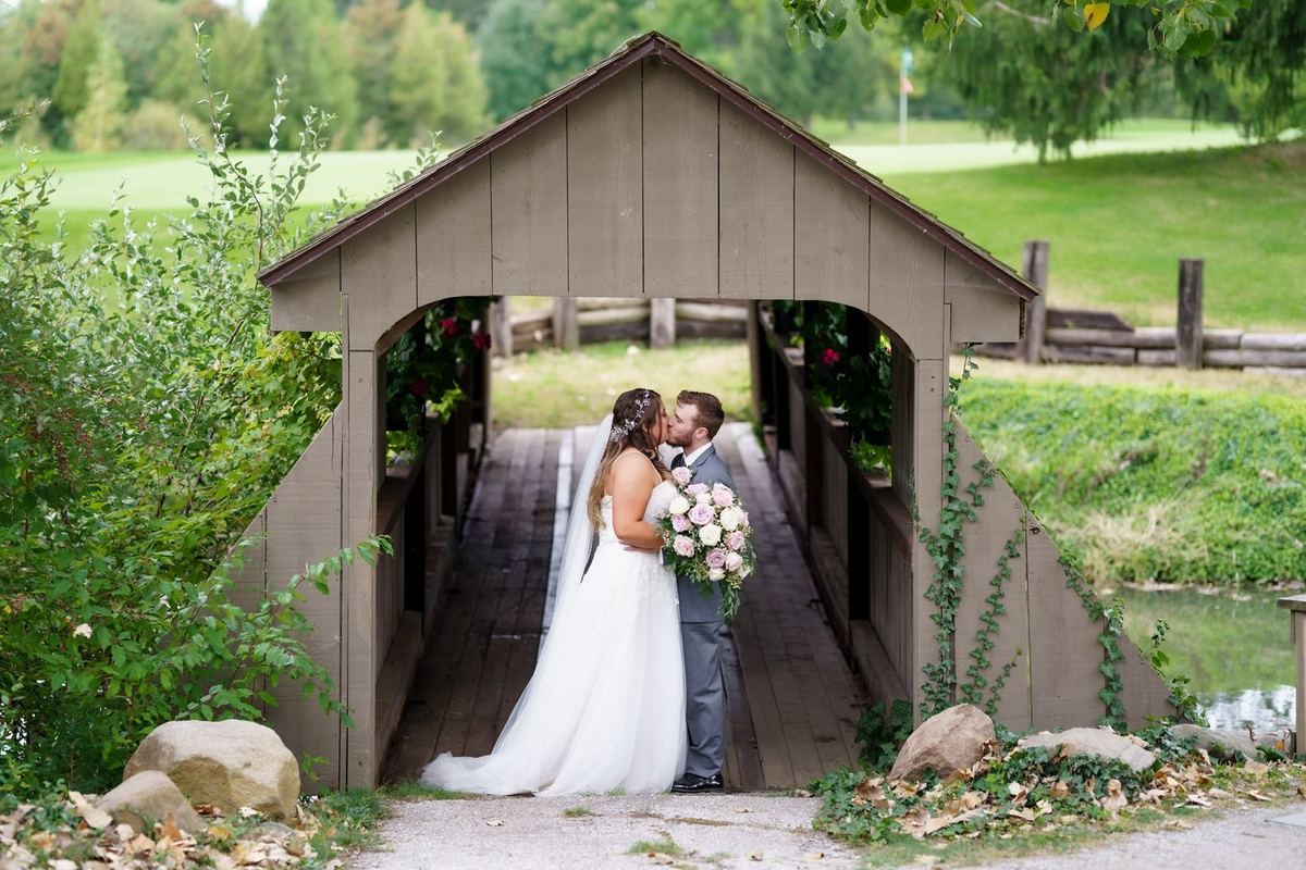Bride and groom standing at the mouth of a covered wooden bridge