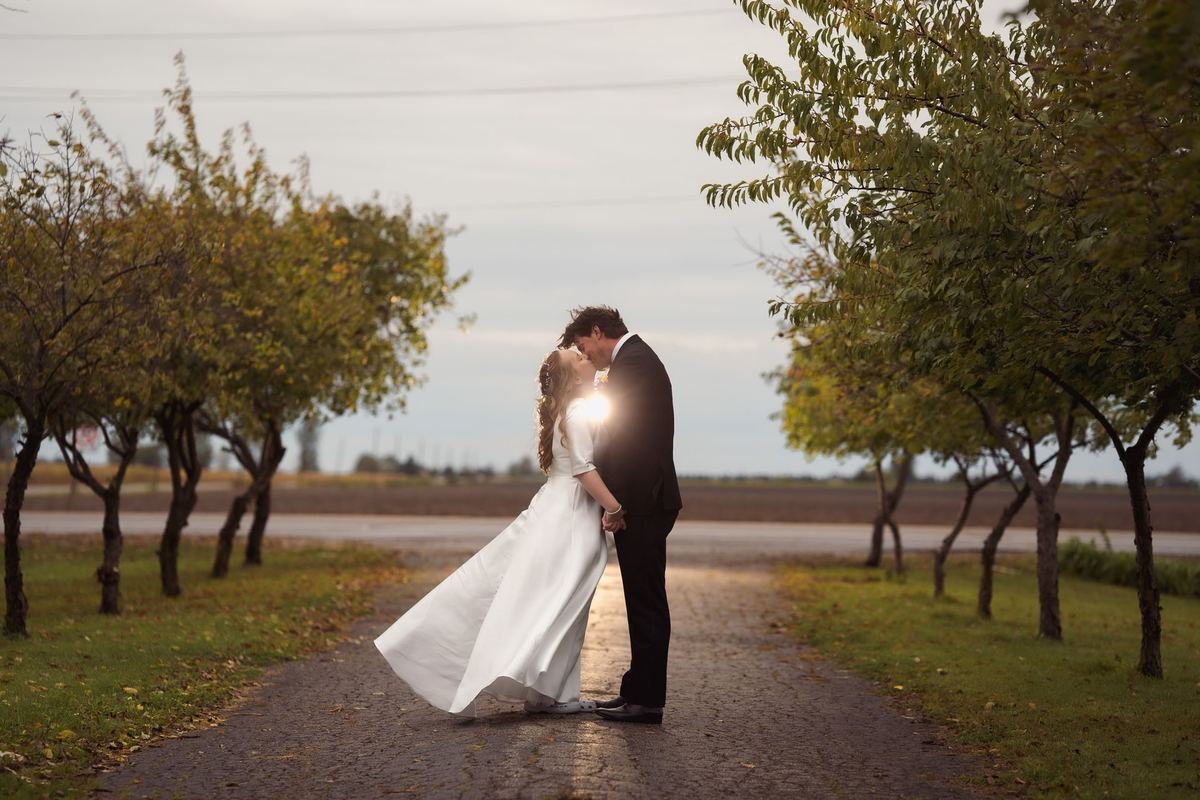 Bride and groom embracing in the middle of a tree-lined laneway