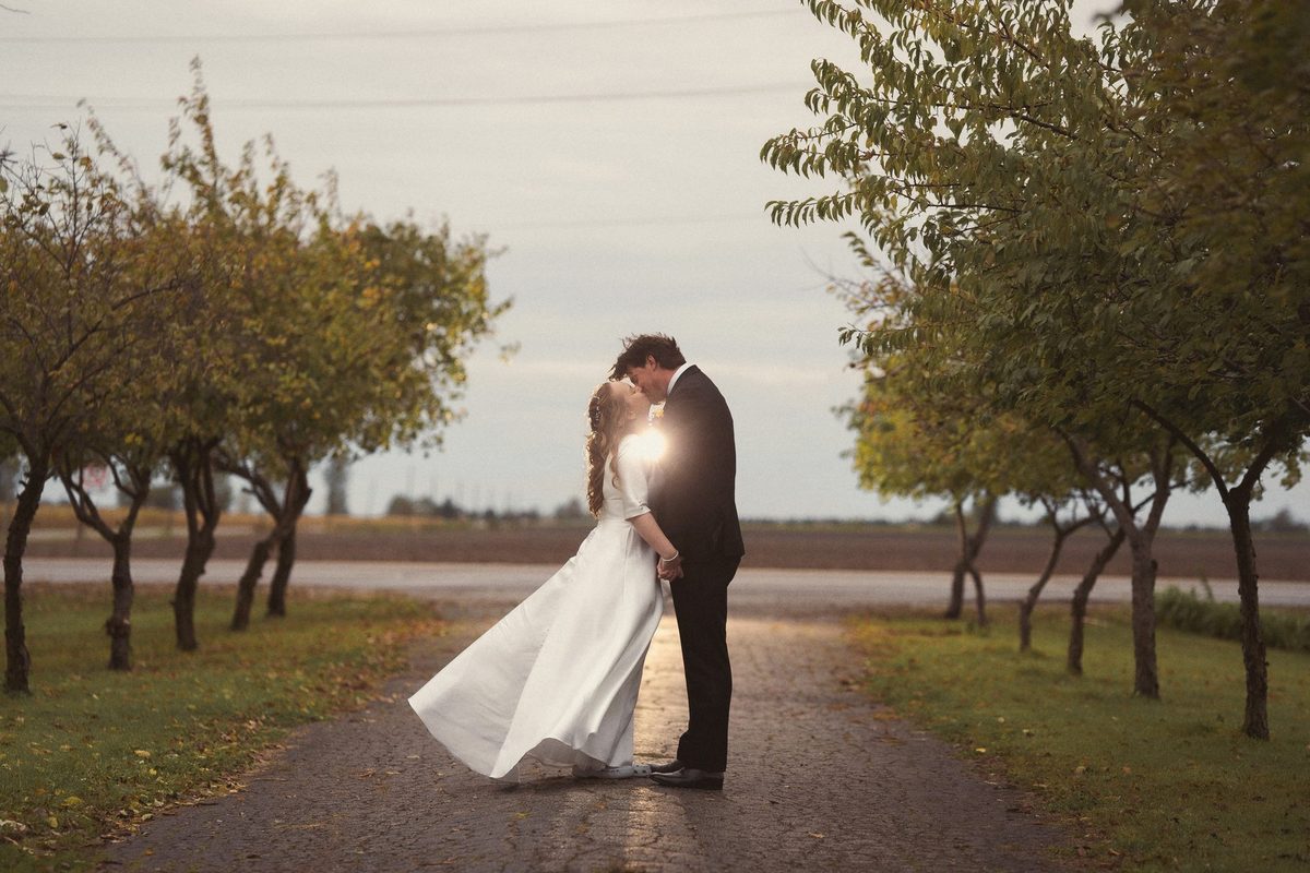 Bride and groom embracing in the middle of a tree-lined laneway
