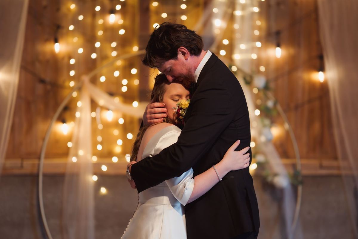 Bride and groom hugging in a barn filled with twinkle lights
