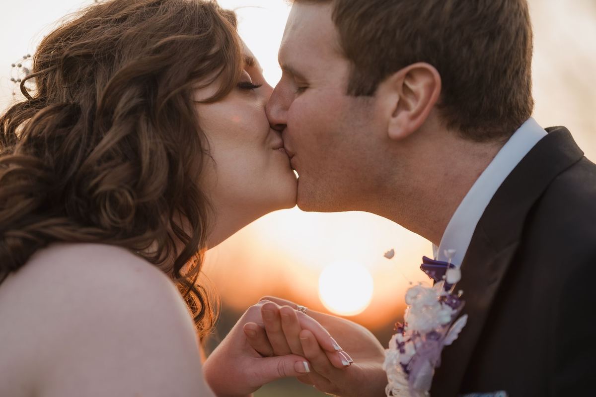 Close-up of the bride and groom kissing with the sun setting behind them