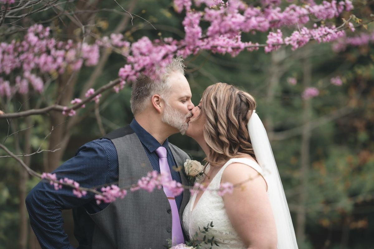 Bride and groom kissing under pink redbud blossoms