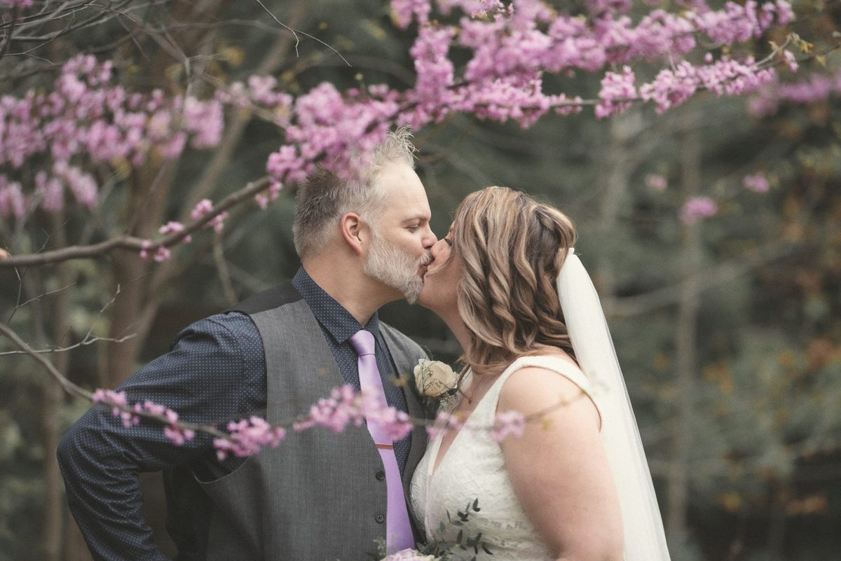 Bride and groom kissing under pink redbud blossoms