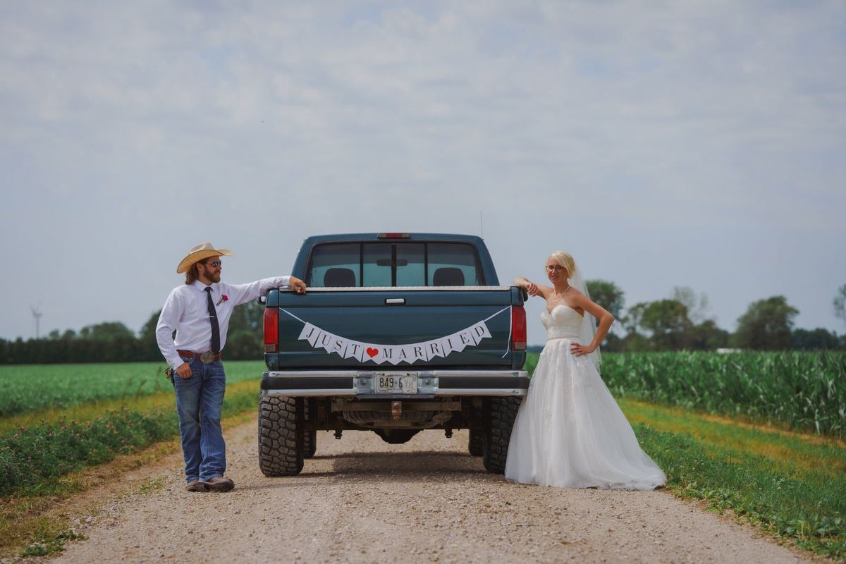 Bride and groom on either side of a pickup truck on a country road