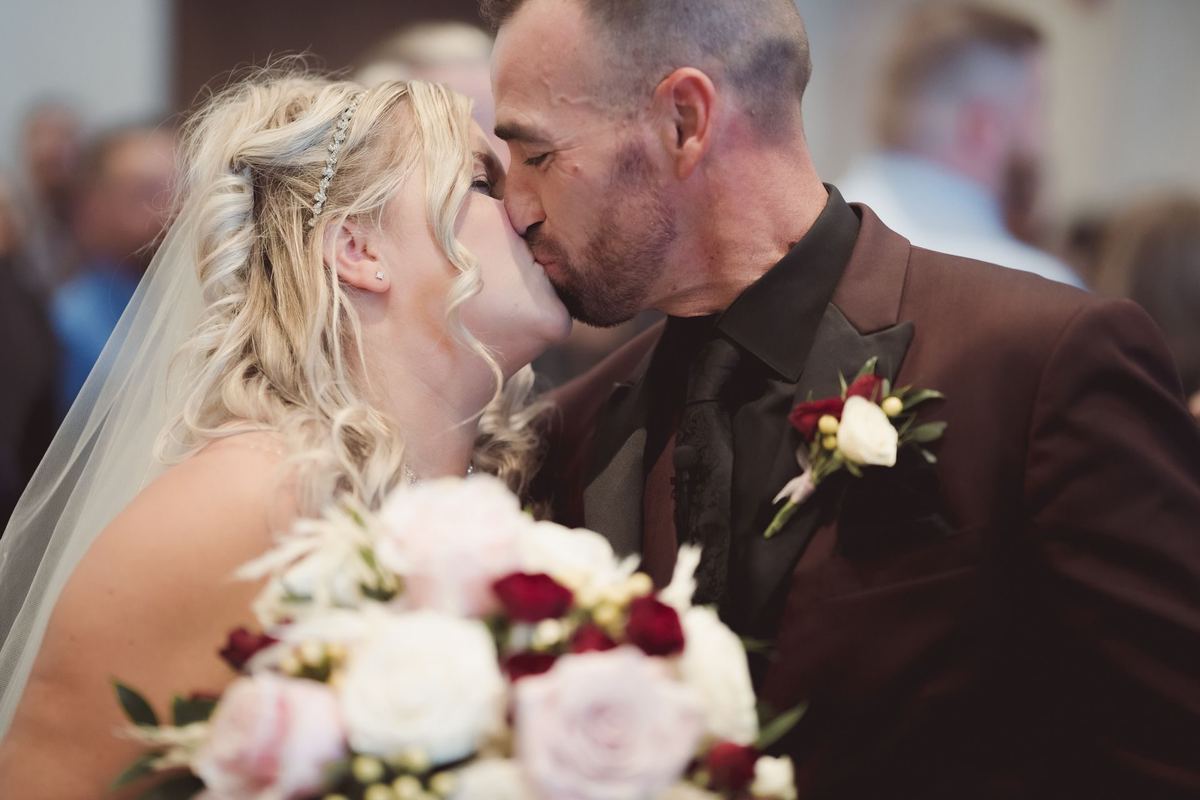 Bride kissing her groom while holding a blush and white rose bouquet