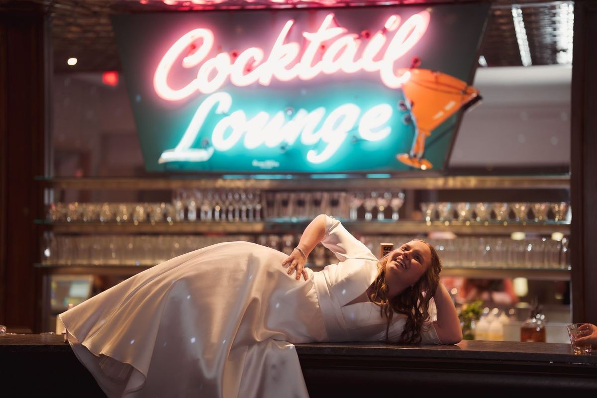 Bride lying across the bar laughing under the cocktail lounge neon at the Retro Suites