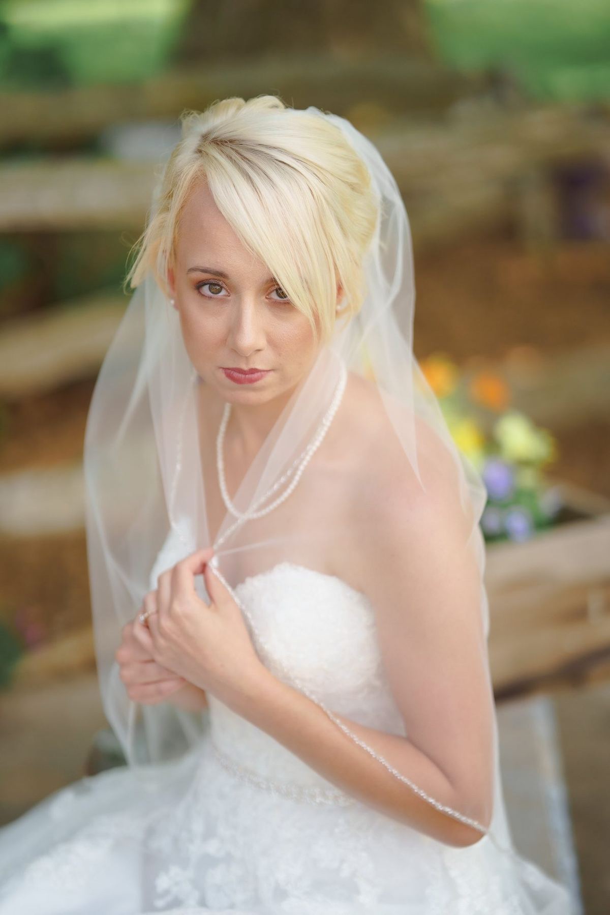 Bride in a veil looking down beside a wooden fence