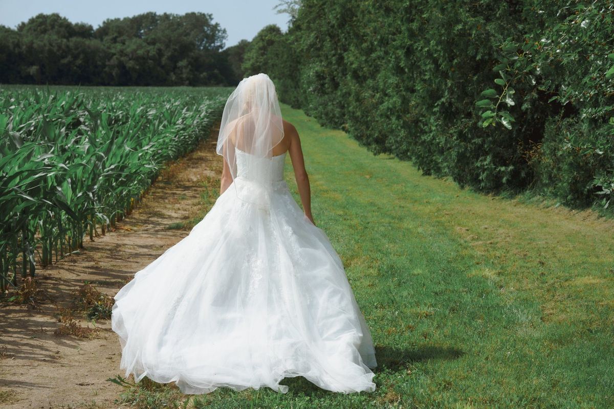Bride walking along a grassy field path in her gown