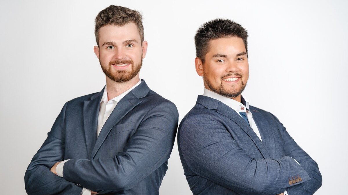 Two business partners in suits standing back to back with arms crossed against a white backdrop, a team photo from a professional headshot session in Chatham-Kent