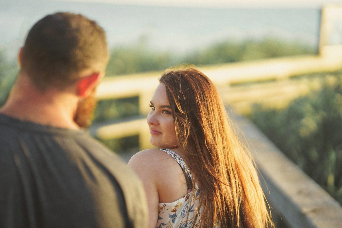 Engaged woman smiling at the camera over her fiancé's shoulder by a wooden railing
