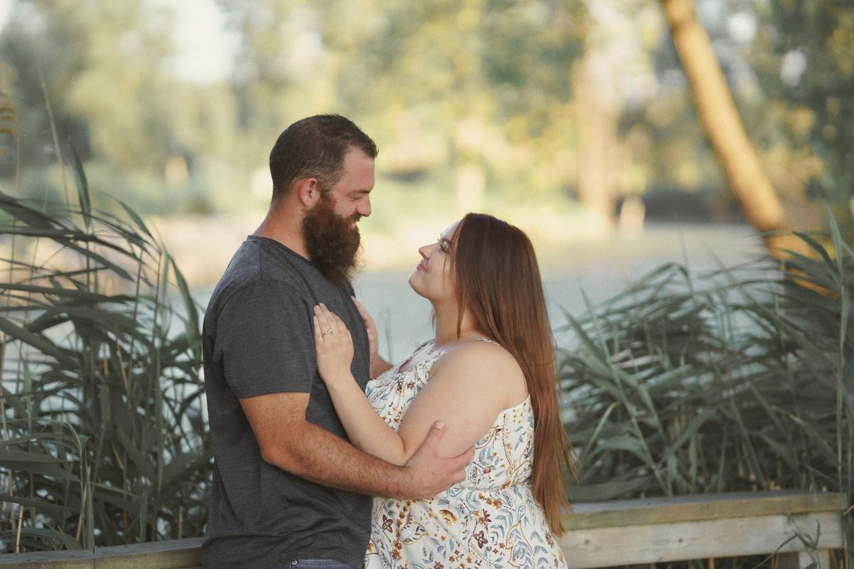 Engaged couple embracing and smiling at each other by tall reeds at Mitchell's Bay