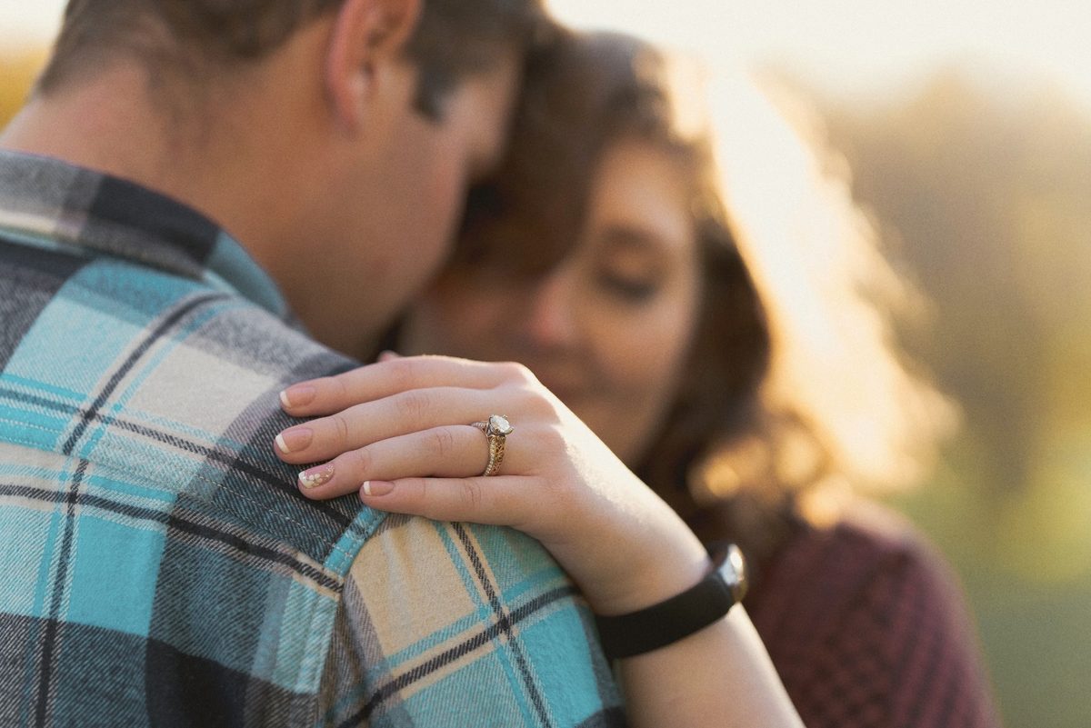 Close-up of an engaged couple cheek to cheek, her engagement ring resting on his plaid shirt