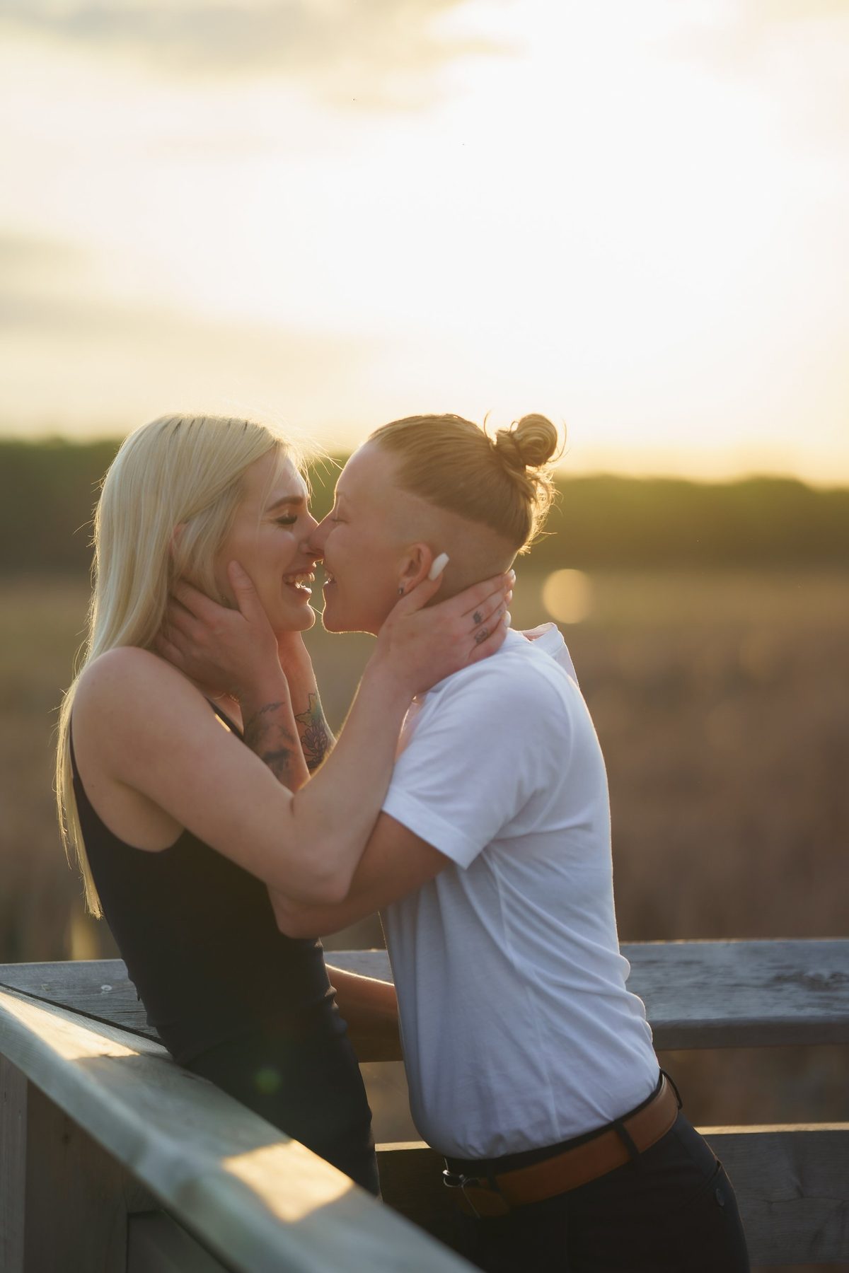 Couple about to kiss by a wooden railing, warm evening sun glowing behind them