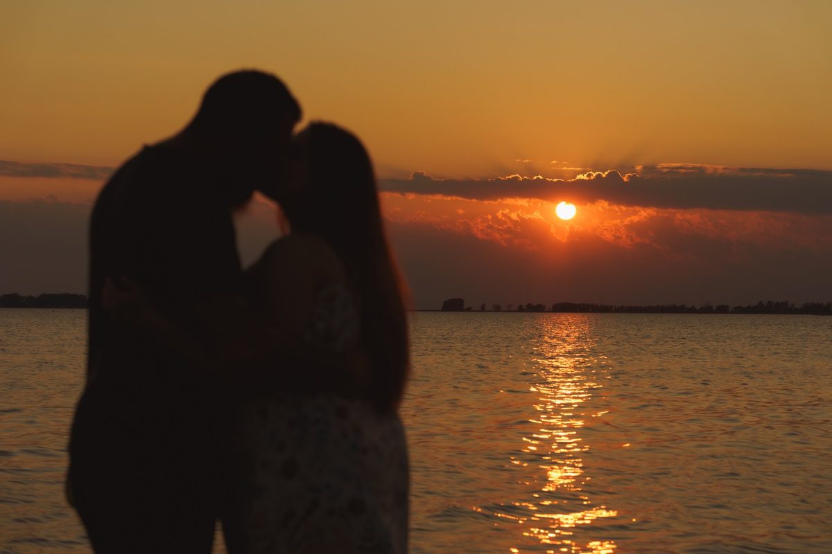 Silhouette of an engaged couple kissing as the sun sets over the lake