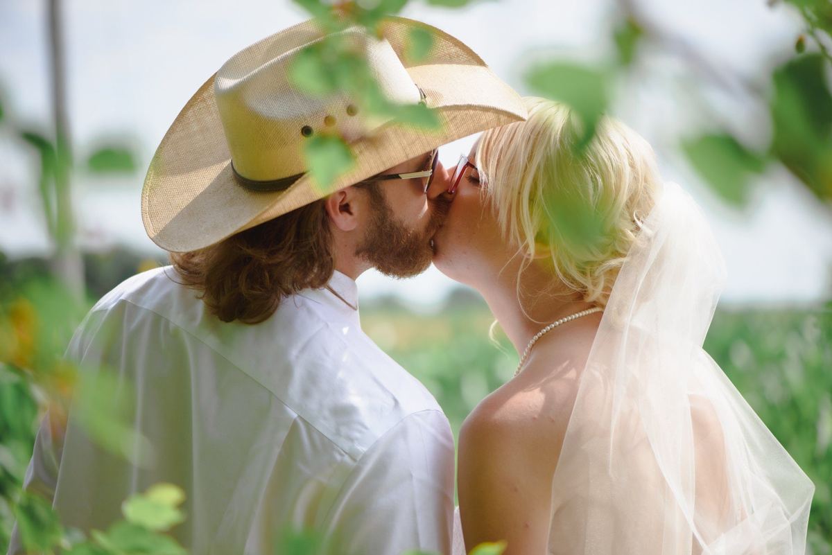 Groom kissing the bride under the brim of his cowboy hat