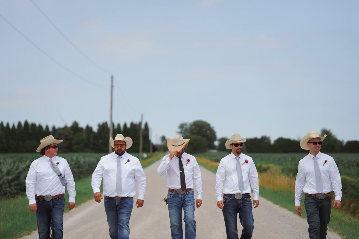 Groomsmen in cowboy hats walking down a country road