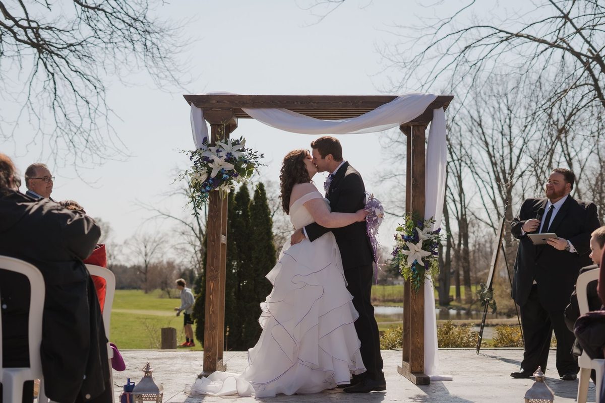 Couple exchanging vows under a wooden arbor at an outdoor ceremony at Links of Kent Golf Club
