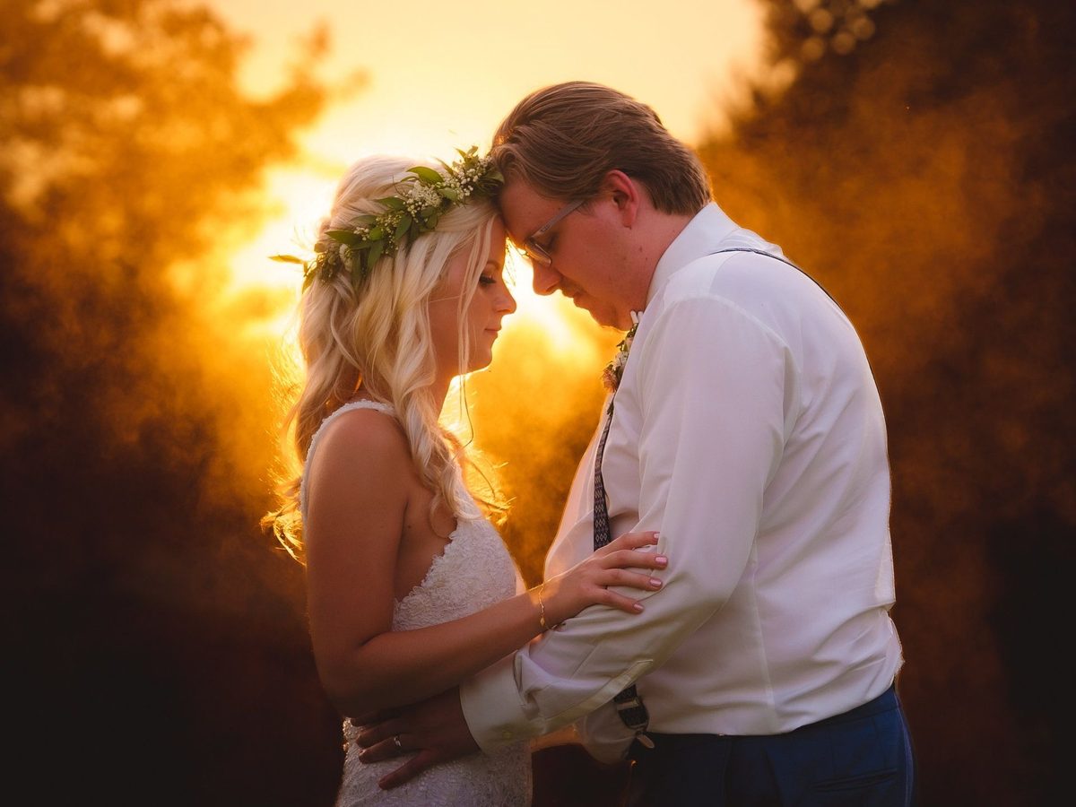 Bride in a flower crown touching foreheads with the groom, glowing golden backlight behind them