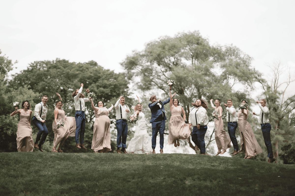 Wedding party jumping and celebrating in a field under big trees