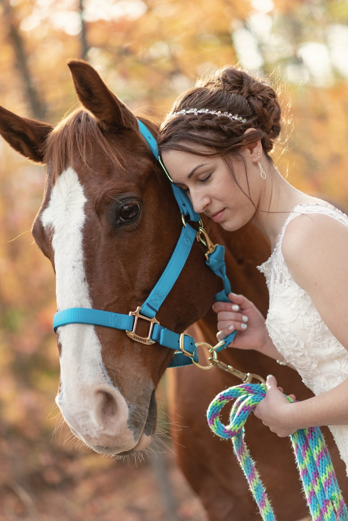 Bride resting her face against a horse's head in warm autumn light