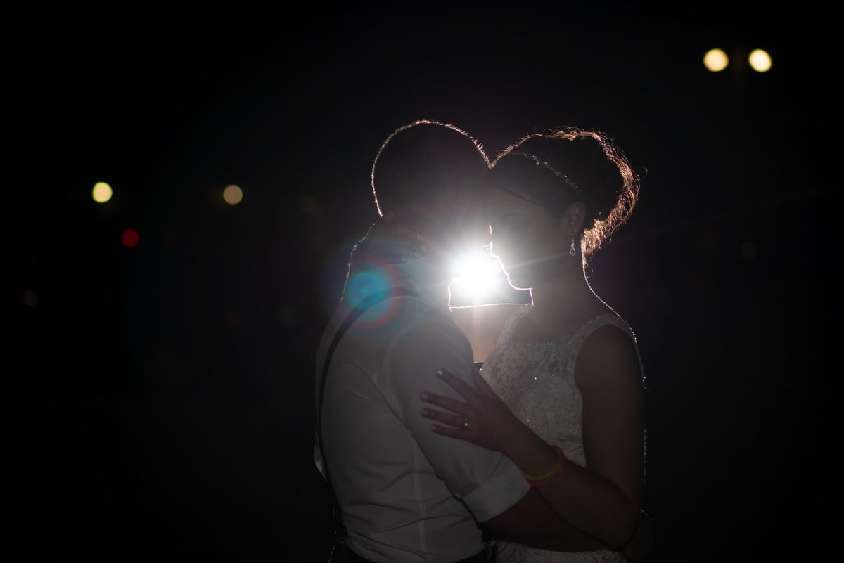 Bride and groom leaning in for a kiss at night with a bright light flaring between them