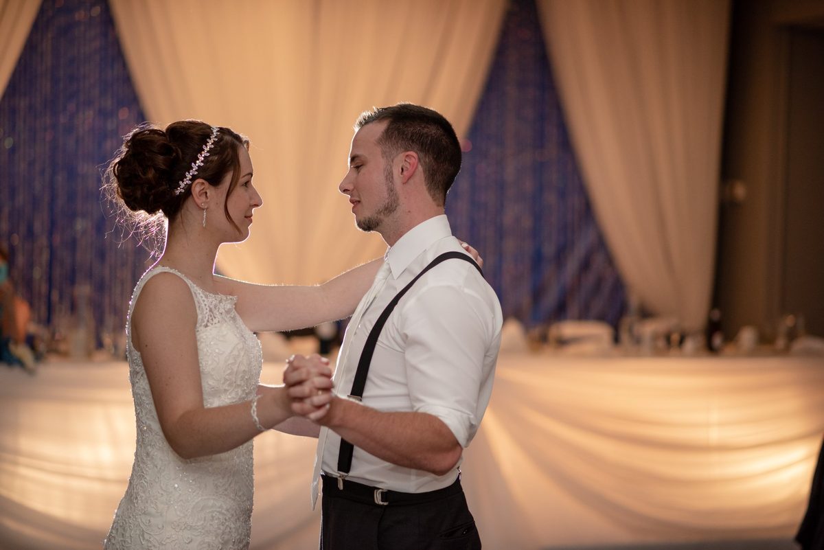 Bride and groom holding hands for their first dance under draped reception lights