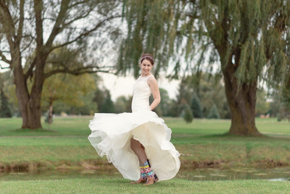 Bride kicking up her gown in a grassy field under big willow trees