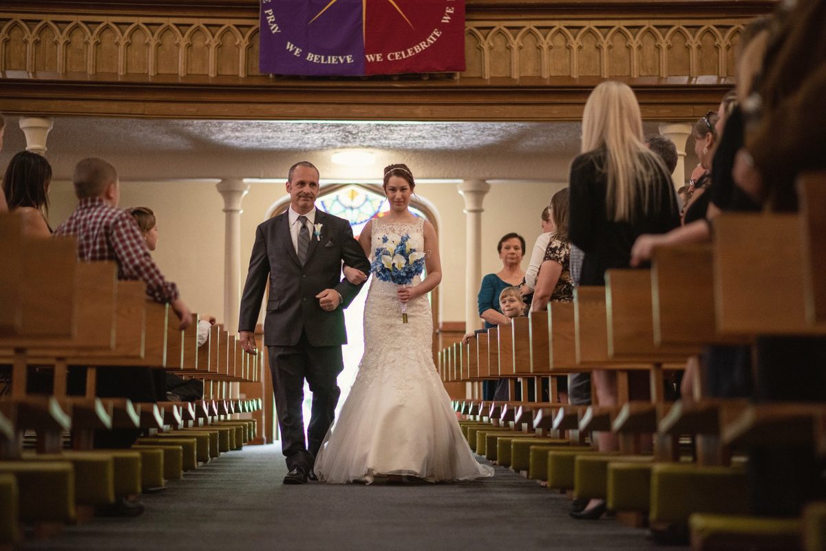 Bride walking down a wooden-pew church aisle on the arm of her escort