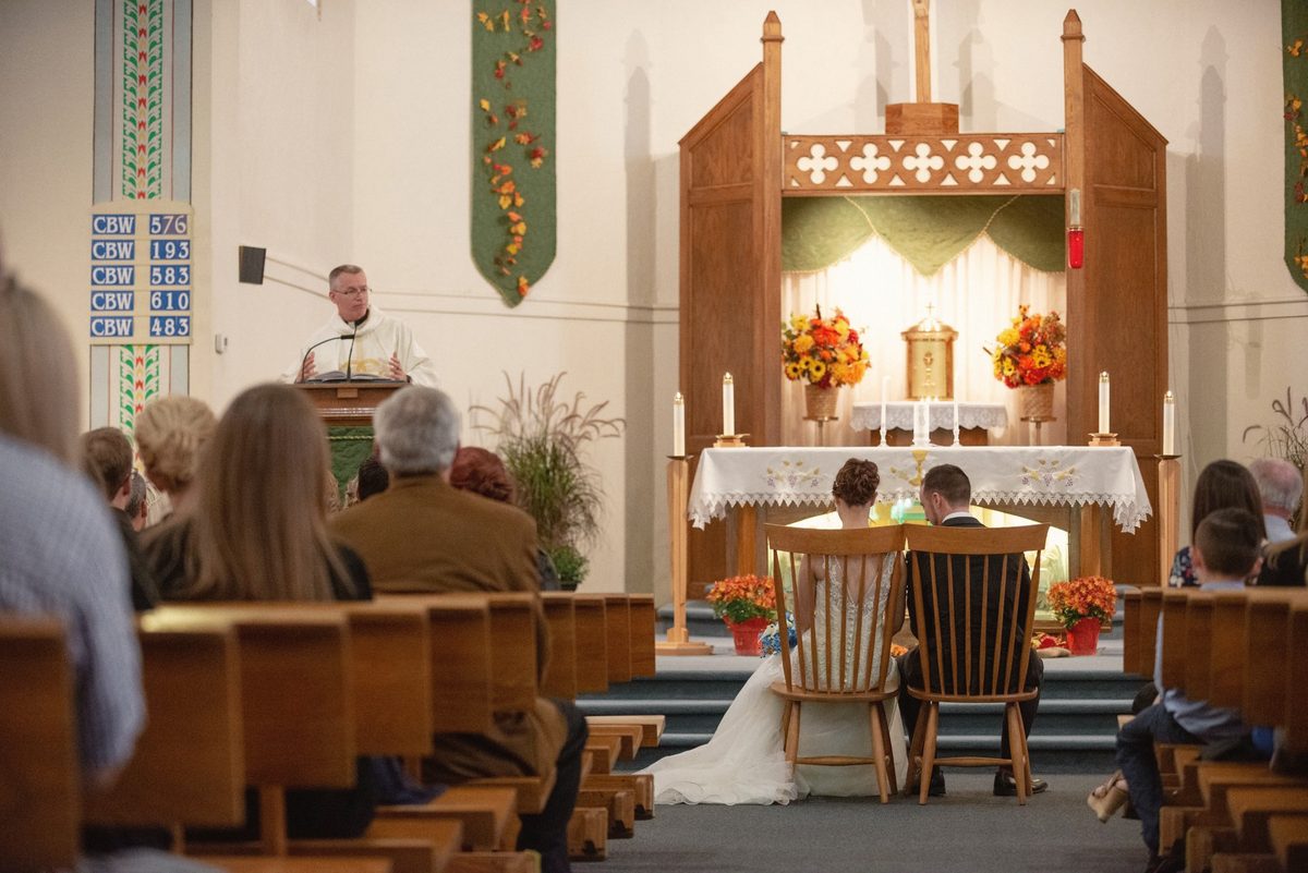 Wide view of the ceremony at the front of a church decorated with autumn flowers