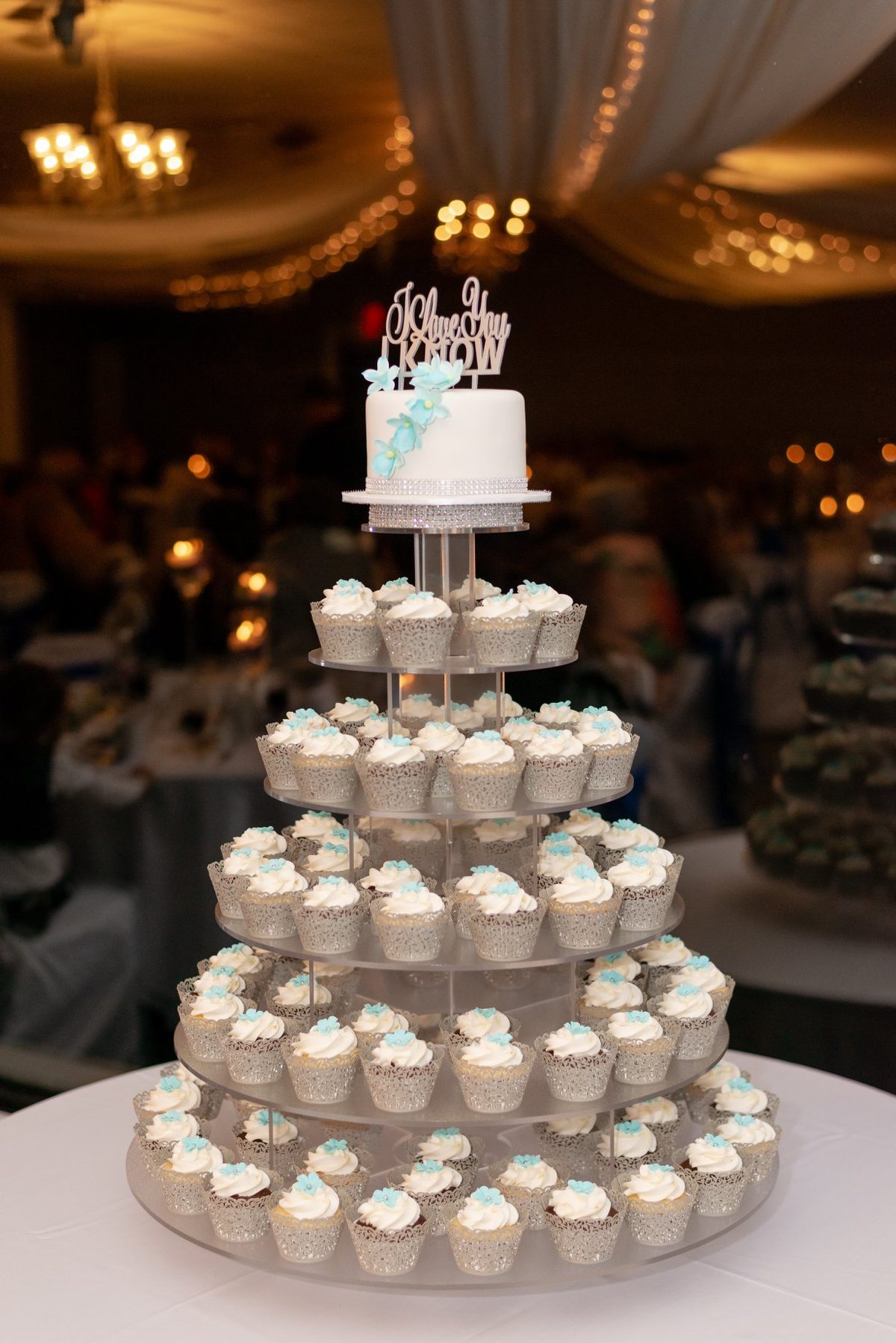 Tiered wedding cupcake tower topped with a small cake under the reception lights