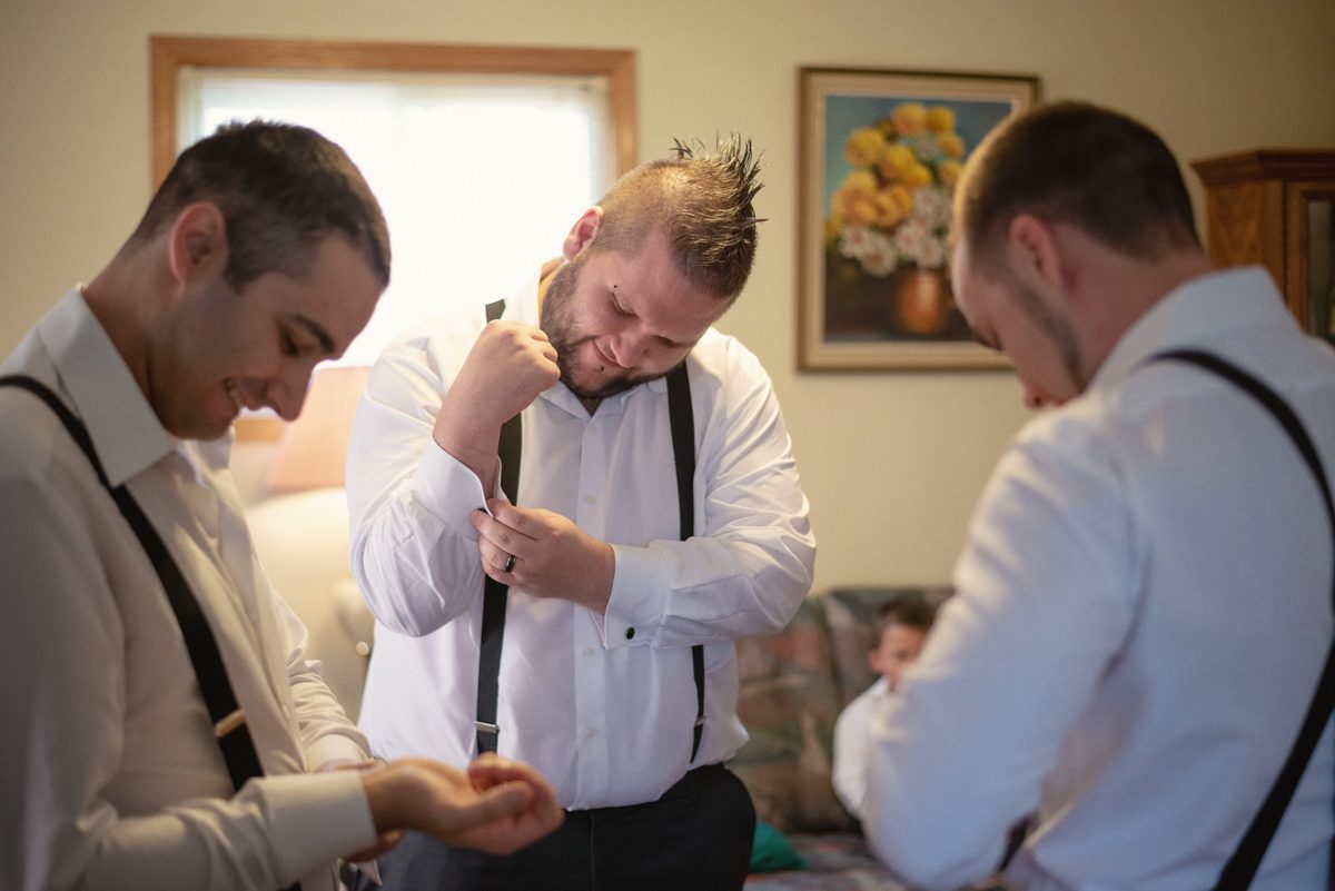 Groom adjusting his shirt and suspenders while his groomsmen get ready beside him