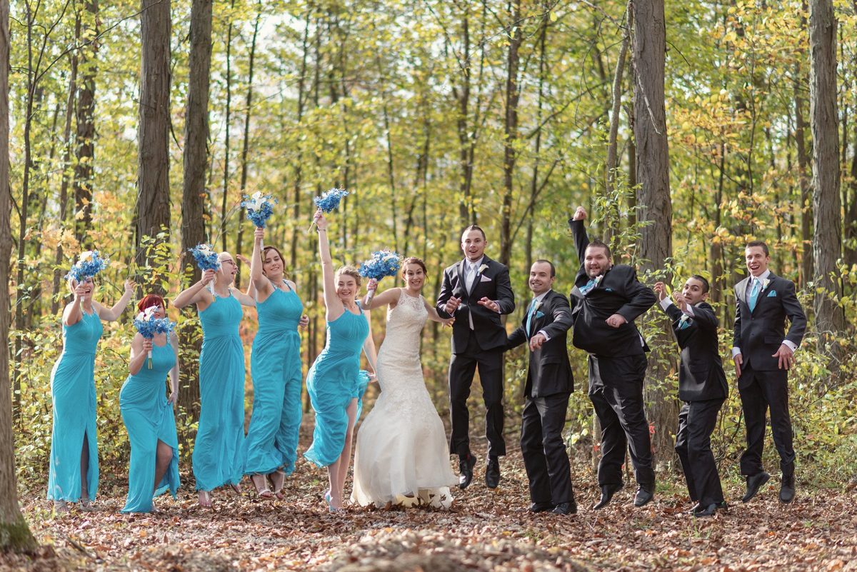 Full wedding party posing playfully among fall trees