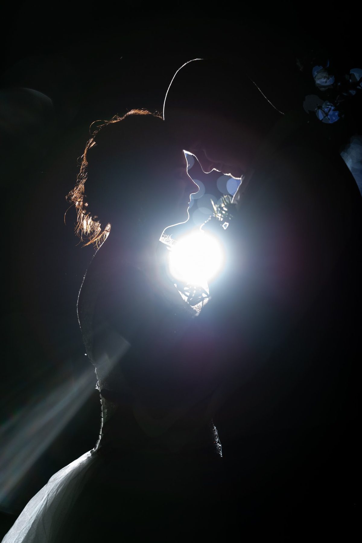 Bride and groom close together at night, a bright light bursting from behind them