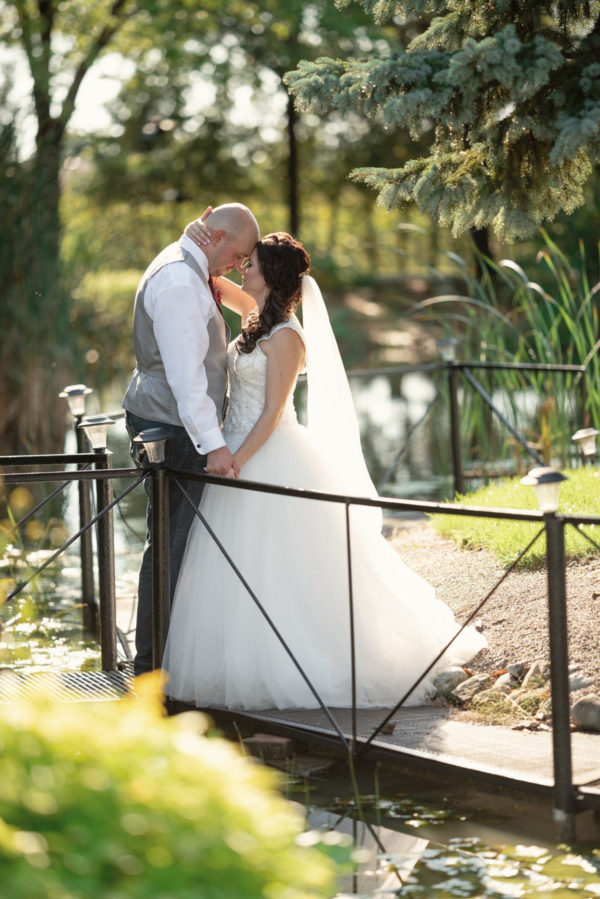 Bride and groom kissing by a black railing over a garden pond