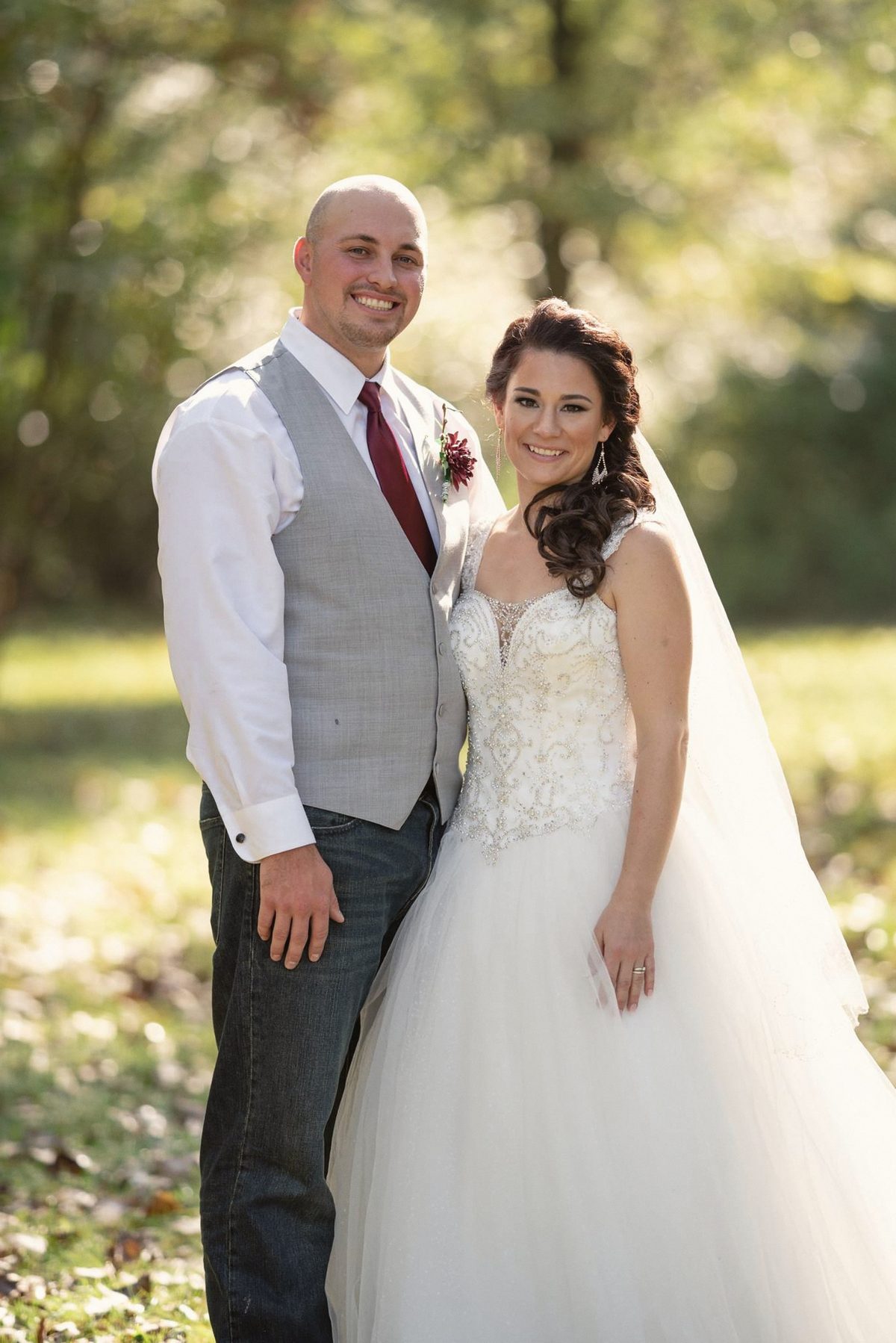 Bride and groom standing close together in front of green trees