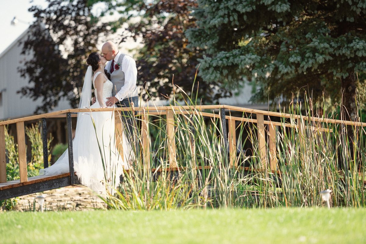 Bride and groom standing on a rustic wooden footbridge among tall grasses
