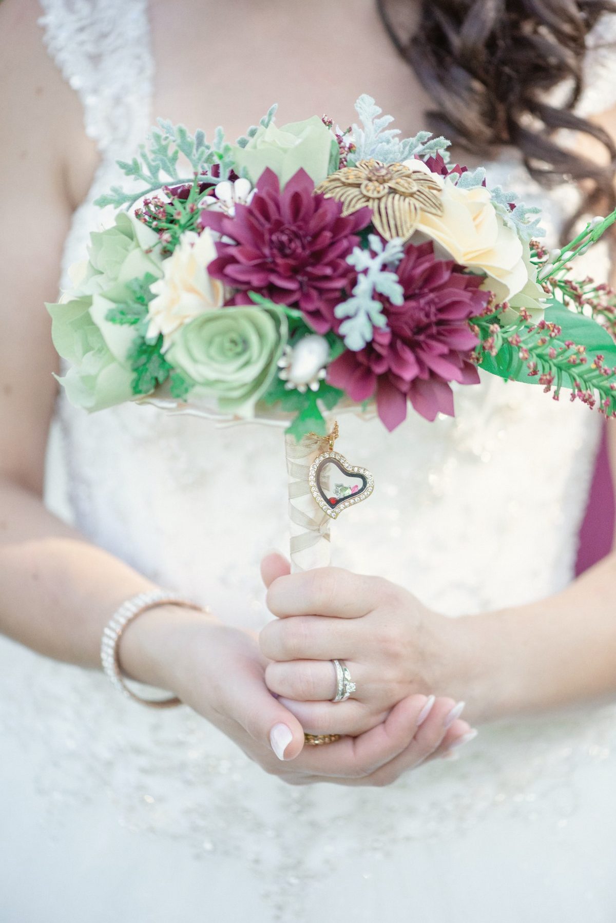 Bride's hands holding a bouquet of burgundy dahlias and green roses against her gown