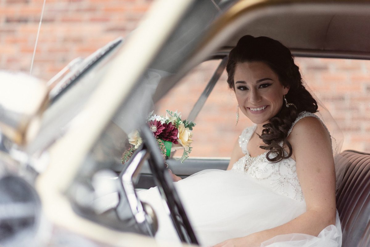 Bride smiling from the driver's seat of a vintage car