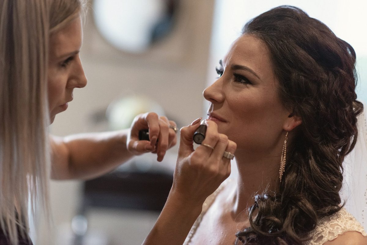 Makeup artist touching up the bride's lips as she smiles
