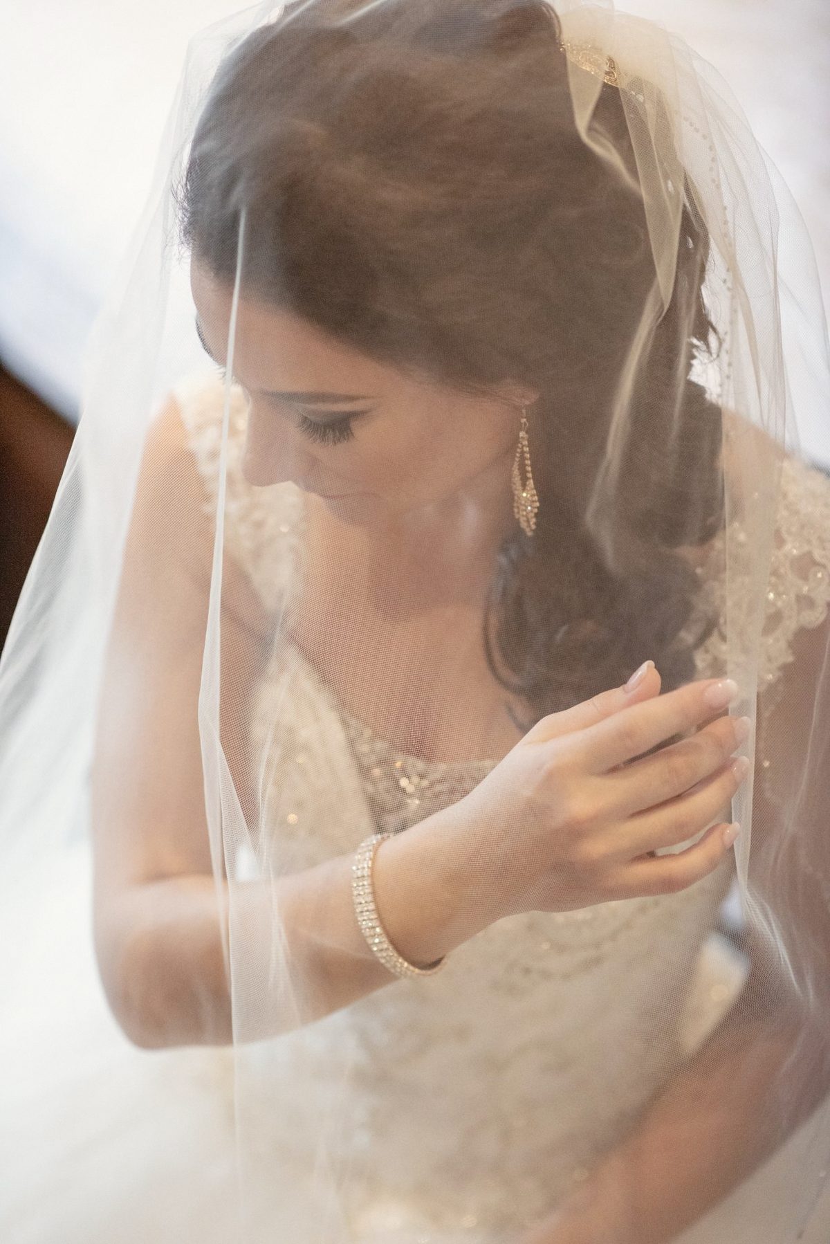 Bride under her veil fastening a bracelet in soft window light