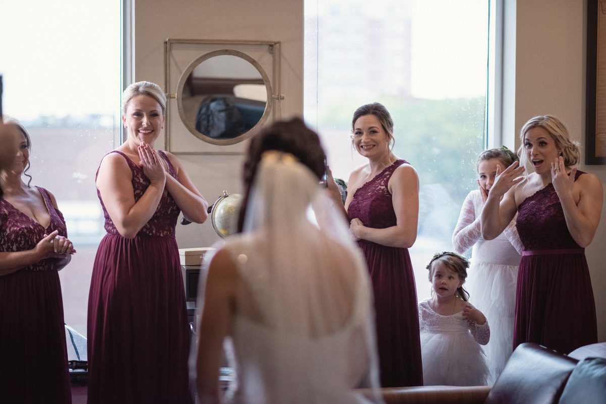 Bridesmaids in burgundy reacting as they see the bride in her gown