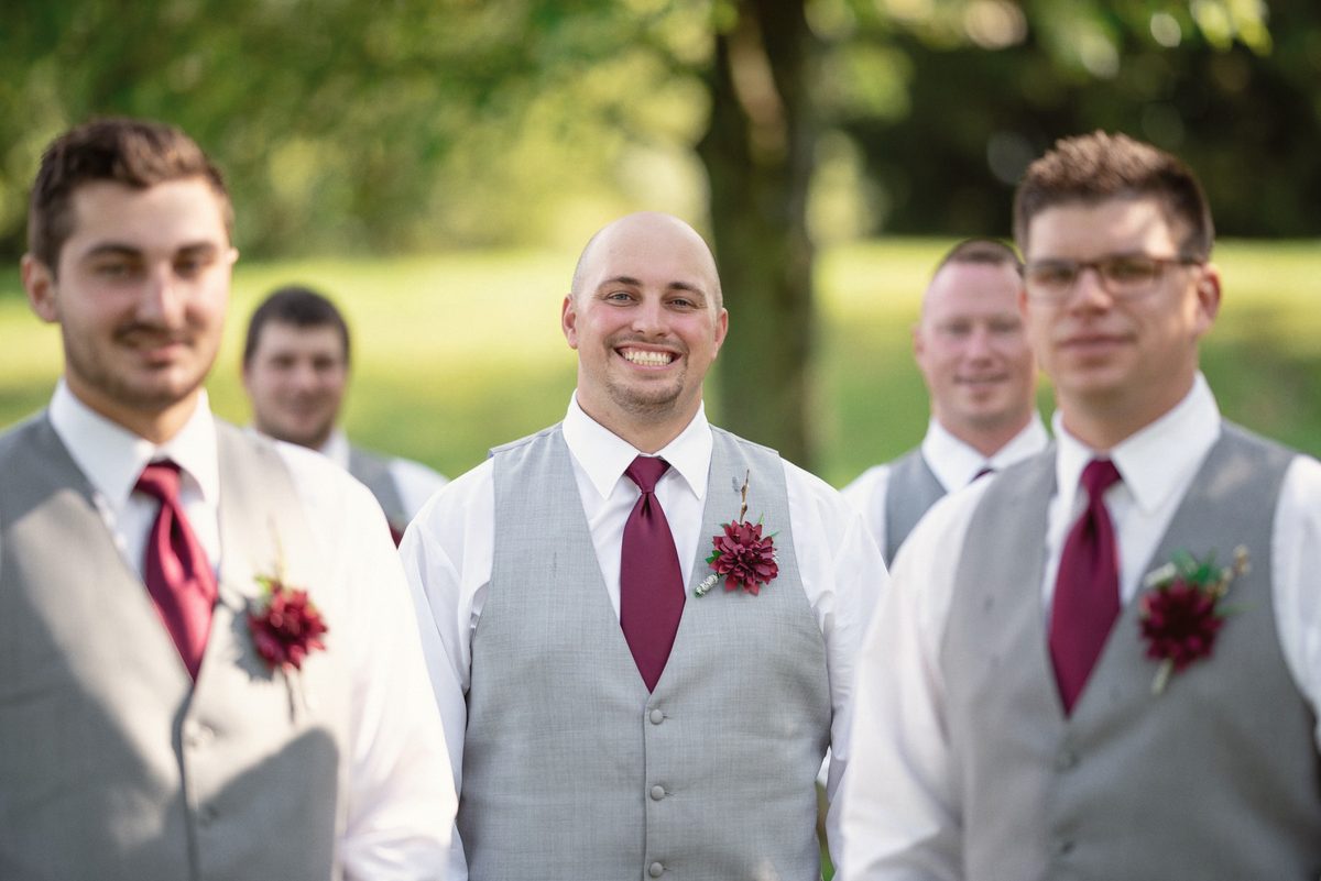 Groomsmen in grey vests and burgundy ties smiling together
