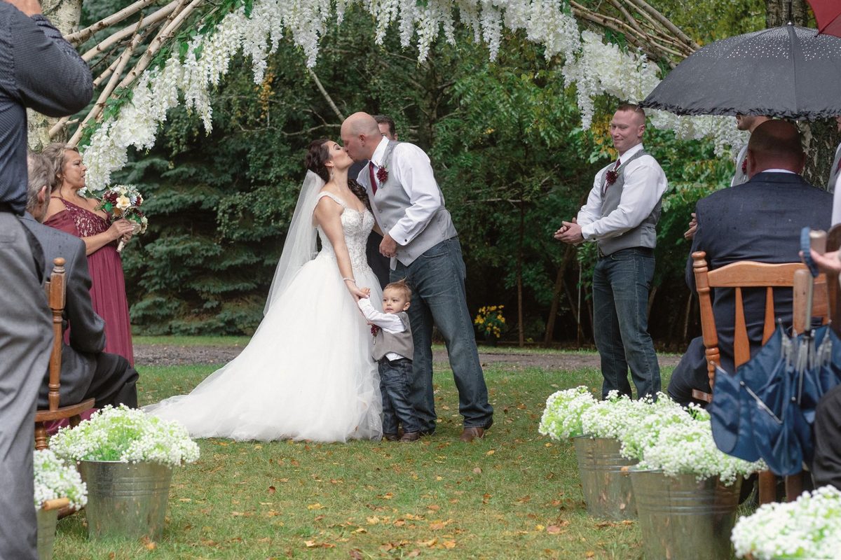 Bride and groom sharing their first kiss at an outdoor ceremony among greenery and guests