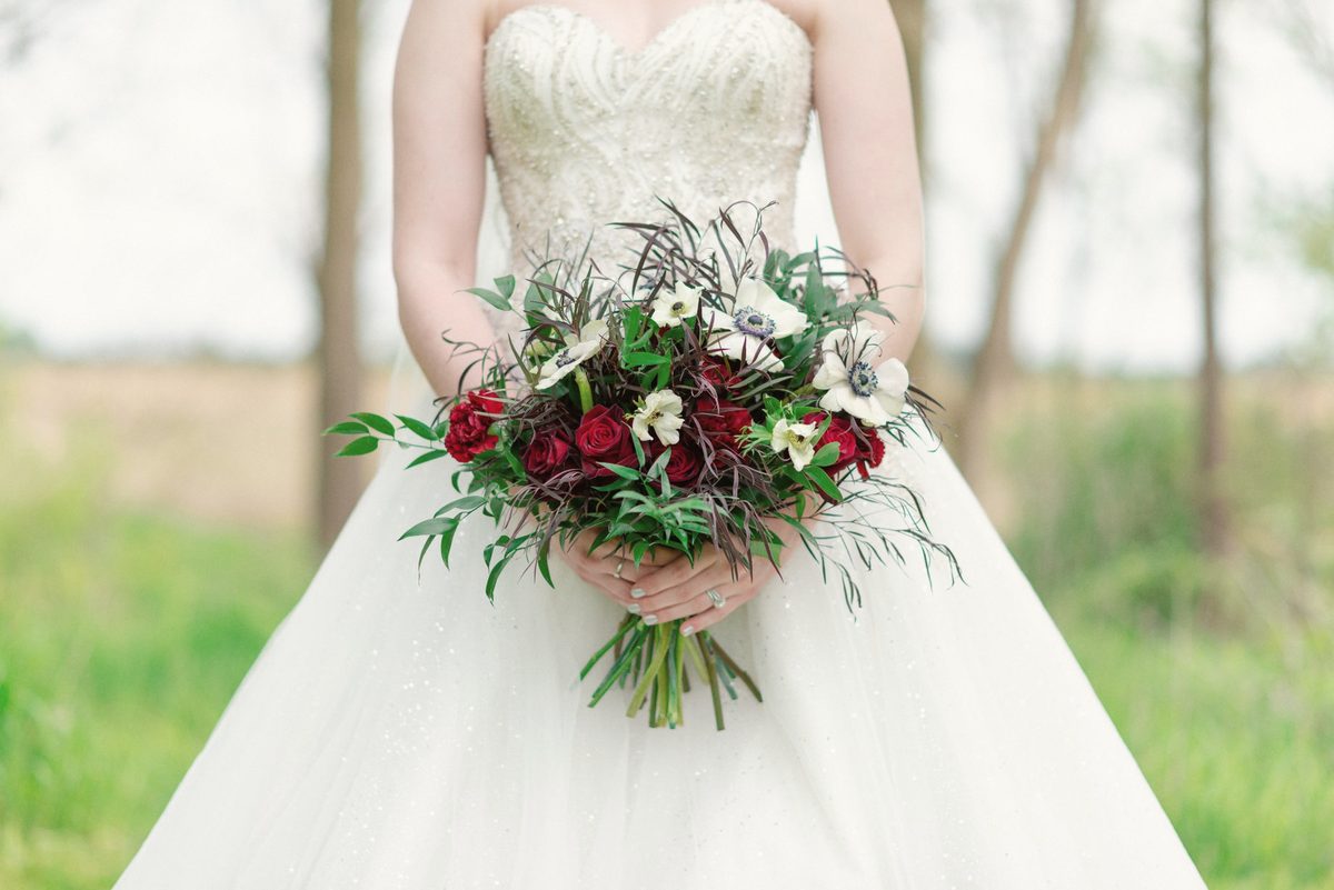Bride holding a bouquet of burgundy and white roses against her gown