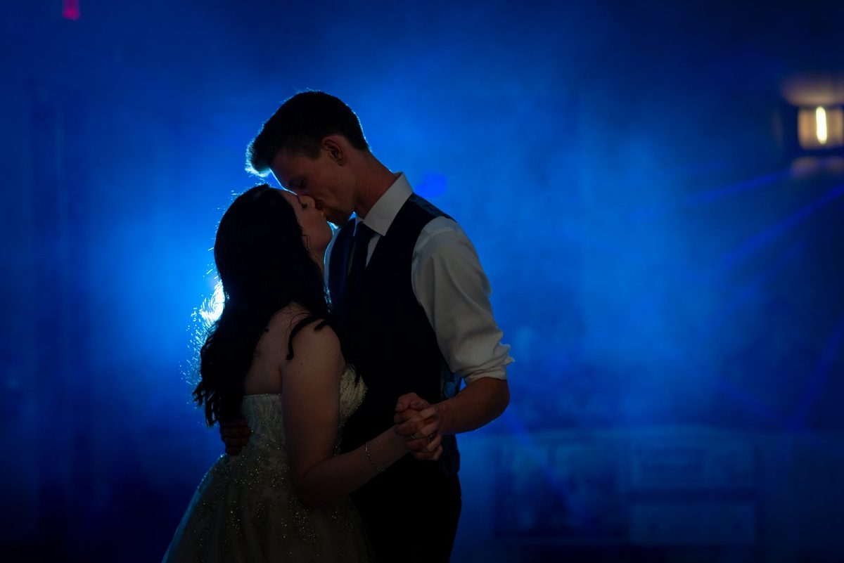 Bride and groom close together against a deep blue backlit glow at night