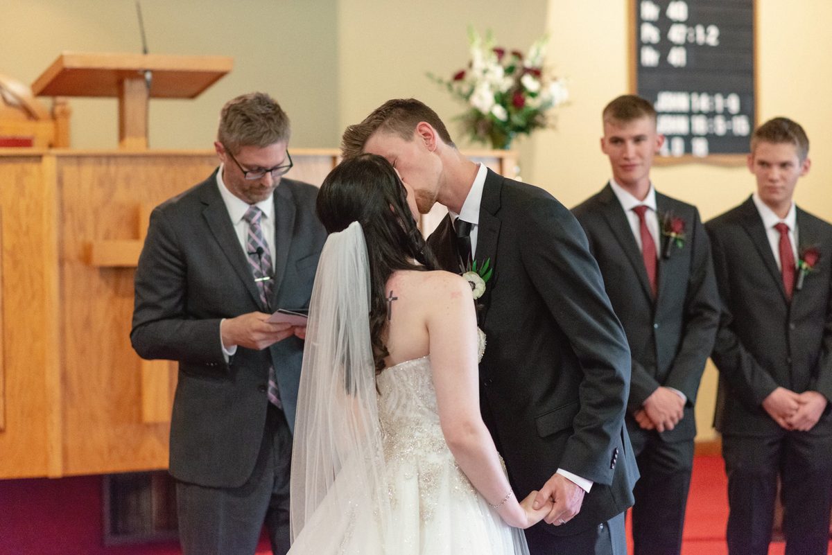Bride and groom kissing at the front of the church with the groomsmen beside them