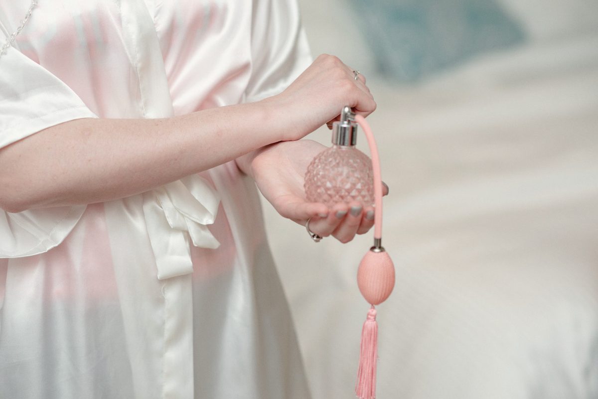 Close-up of the bride in a satin robe spritzing perfume