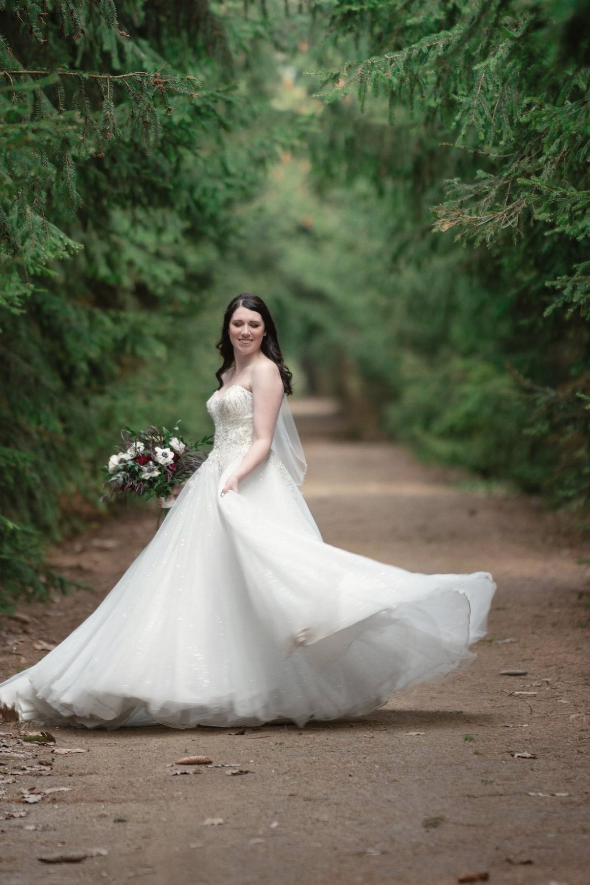 Bride twirling her full gown on a dirt path through the trees